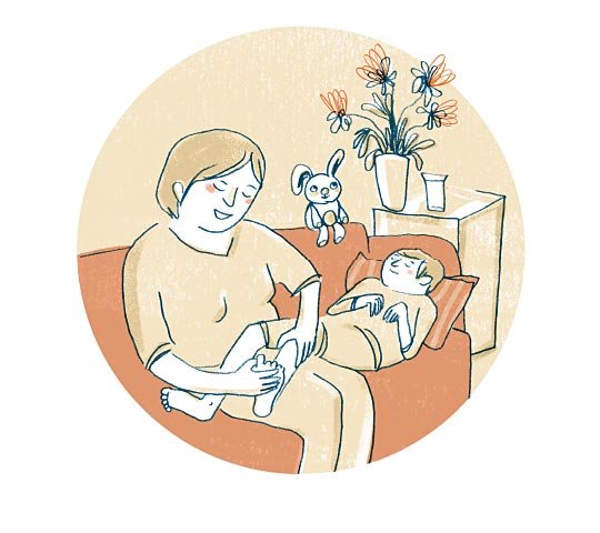 Eine Mutter sitzt auf dem Sofa. Ihr Sohn liegt neben ihr. Seine Beine liegen auf den Oberschenkeln der Mutter. Sie streichelt mit einer Hand die Wade ihres Sohnes. Mit der anderen Hand streichelt sie seine Zehen.